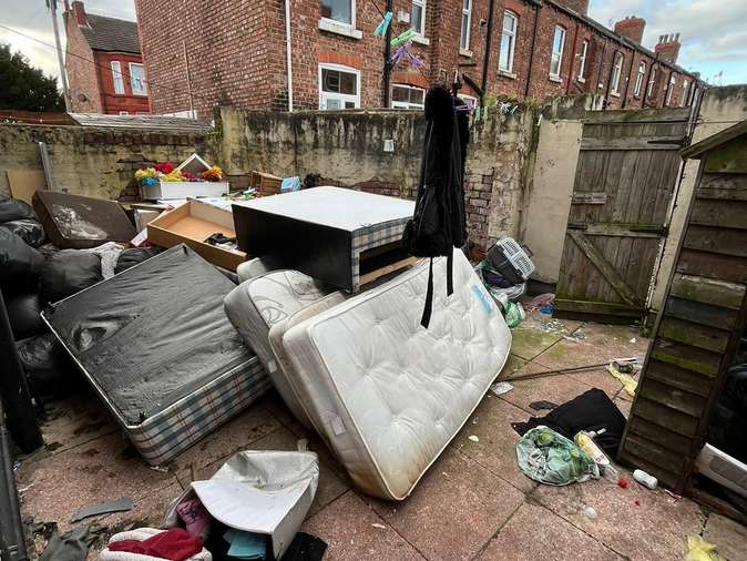 Backyard cluttered with mattresses, furniture and waste before clearance