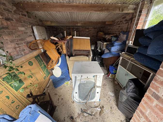 Outbuilding packed with washing machine, chairs and household items before clearance